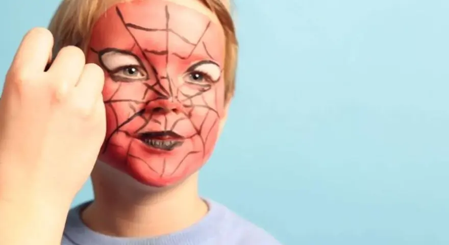 Ein Kind wird mit einem Spiderman-Gesicht bemalt. Rote Farbe und schwarze Spinnennetzmuster verwandeln das Gesicht in eine Superheldenmaske.