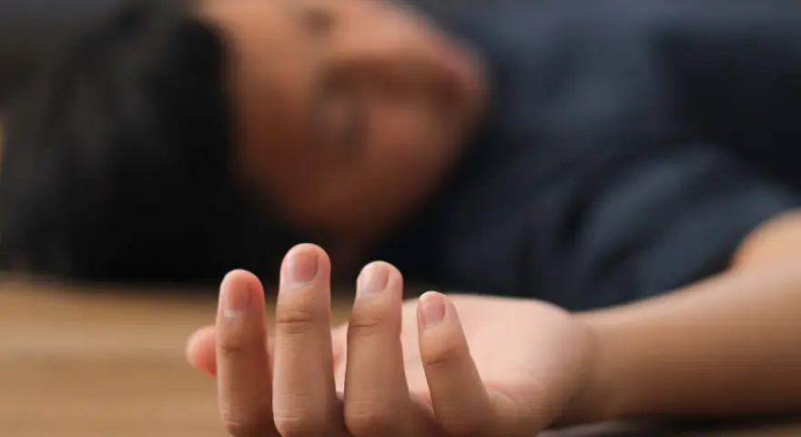 Nahaufnahme einer Hand, die auf dem Boden liegt, während eine Person mit einem epileptischen Anfall bewusstlos ist.