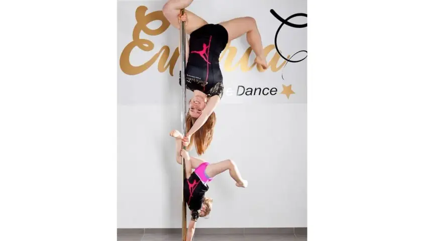 Dwie tancerki, dorosła i dziecko, wykonują akrobacje na słupie. To dowód, że pole dance dla dzieci to świetna zabawa i aktywność.