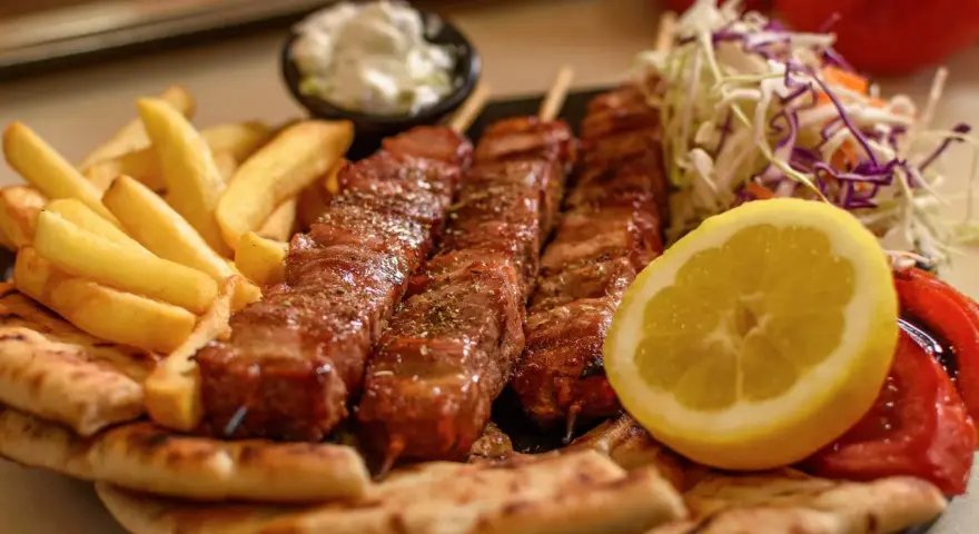Pyszne souvlaki na patykach, podane z frytkami, pitą, surówką i cytryną.