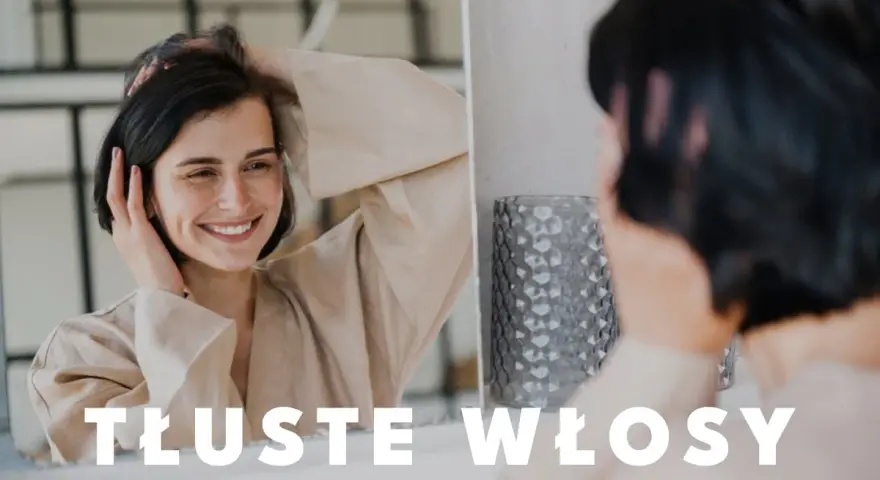 Uśmiechnięta kobieta dotyka swoich włosów, zastanawiając się, co zrobić, żeby włosy się nie przetłuszczały.