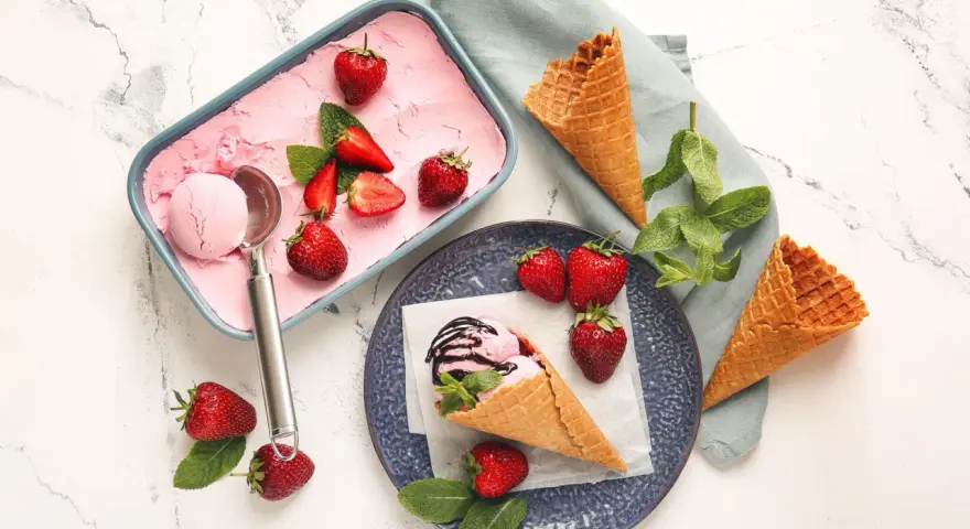 Ein Behälter mit rosa Obst Eis, Erdbeeren und Minze. Ein Eisbecher mit Eis und Schokoladensauce.