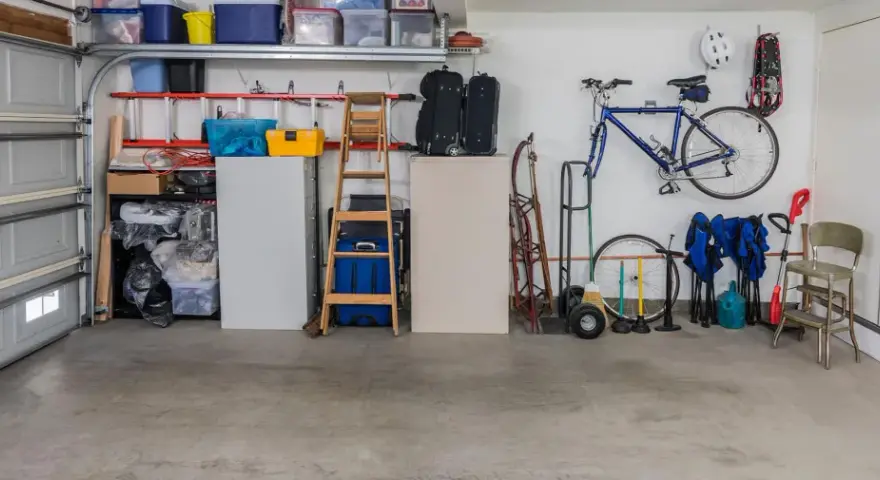 Garage med cykel, stegar, förvaringslådor och en liten fönsterlucka för ventilation.