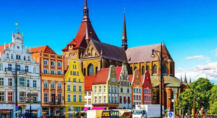 Bunte Giebelhäuser und die Marienkirche prägen das Bild der Rostocker Innenstadt. Ein sonniger Tag auf dem Platz.
