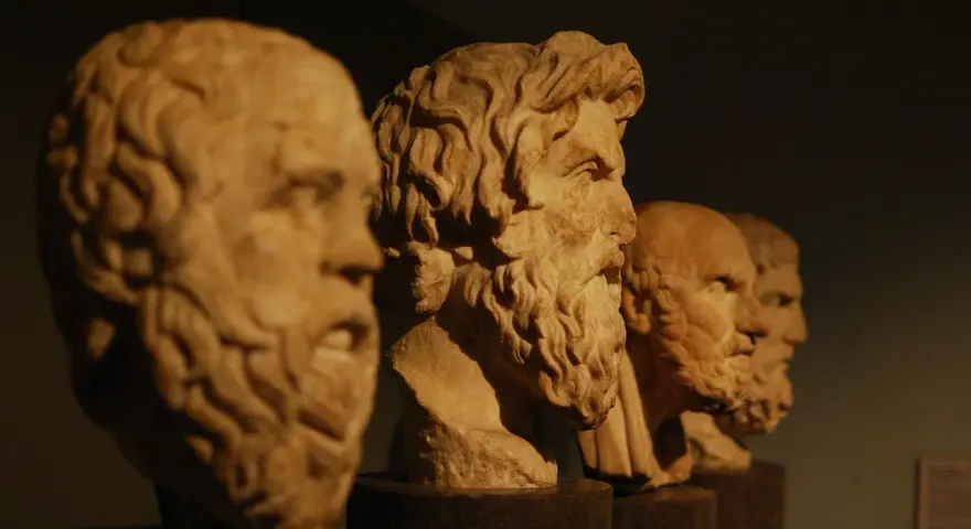 Bustos de mármol de filósofos de la edad antigua Grecia, con barbas y miradas serias, alineados en un museo.