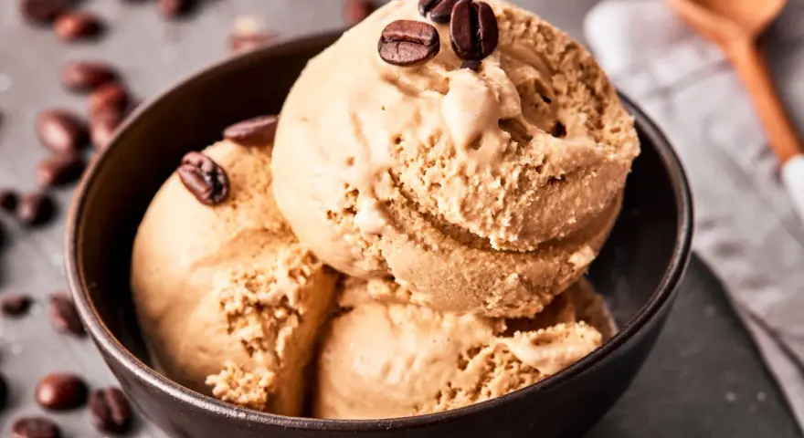 Kaffee Eis in einer Schale, garniert mit Kaffeebohnen. Ein Löffel liegt daneben.