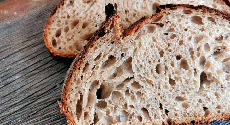 Zwei Scheiben rustikales Sauerteigbrot mit großer Porung liegen auf einem Holzbrett. Die Sauerteig Vorteile sind offensichtlich: ein toller Geschmack und eine bekömmliche Textur.