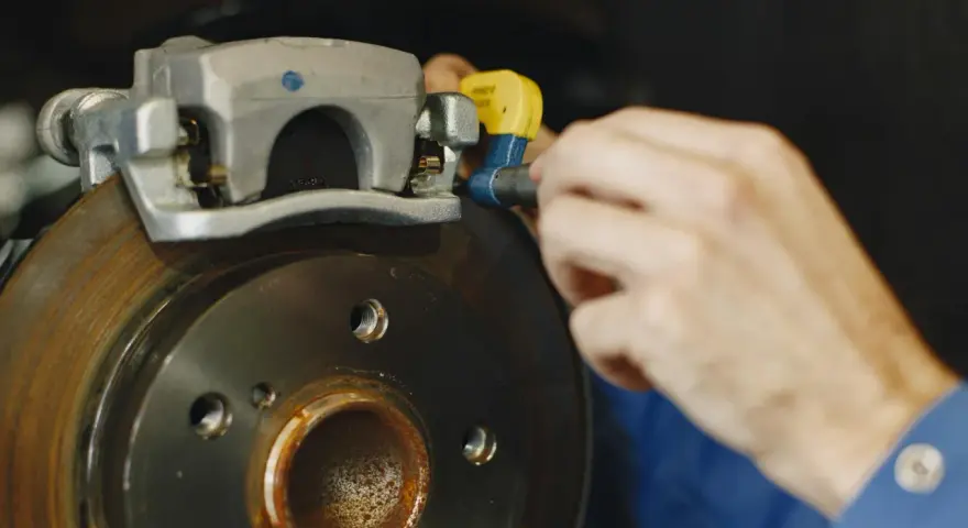 Mechanik dokręca śrubę w jarzmie zacisku hamulcowego, naprawiając układ hamulcowy pojazdu.