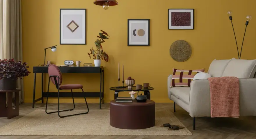 Un salotto con pareti giallo ocra e dettagli tortora. Un divano beige, un pouf tortora e un tappeto in juta creano un'atmosfera accogliente.