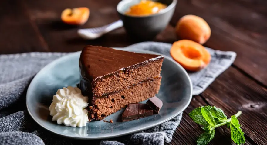 Ein Stück Sachertorte, das aussieht wie vom Original Sachertorte Rezept, mit Schlagobers, Schokolade und Marillenmarmelade.