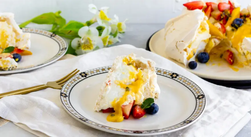 Porción de pavlova con fresas, arándanos y mango, bañada en salsa de maracuyá. Los pavlova ingredientes son visibles en este postre.