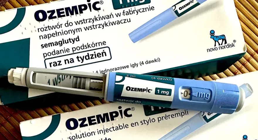 Dwa opakowania i dwa peny leku Ozempic 1 mg na podkładce bambusowej.