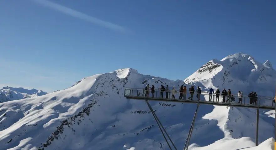 Ludzie na platformie widokowej podziwiają ośnieżone szczyty Alp, jakby byli w świecie Grindelwalda.