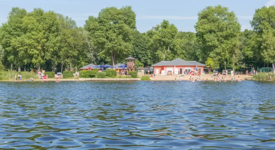 Sommerfreuden am See in Berlin: Menschen planschen im Wasser, entspannen am Strand und genießen die Sonne.