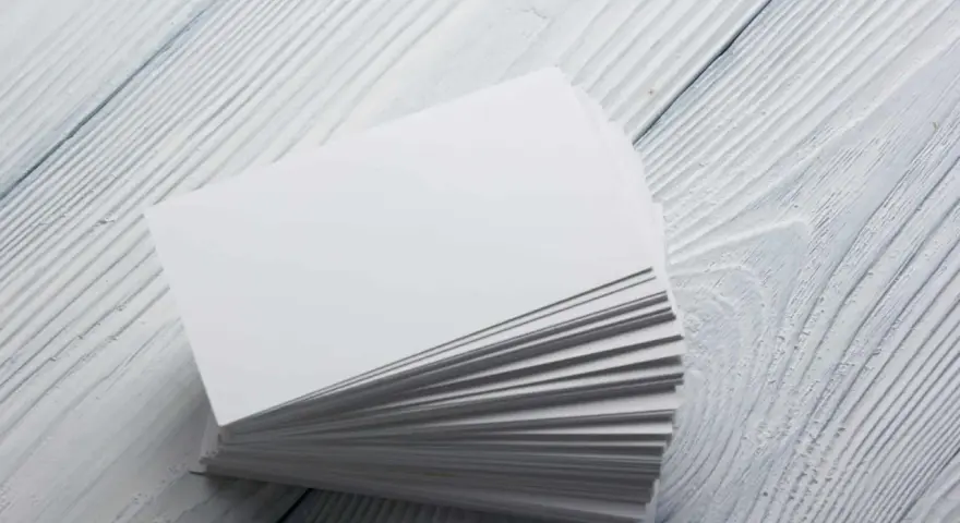 Stos białych wizytówek, idealnych na papier satynowy lub kredowy, leży na drewnianym blacie.