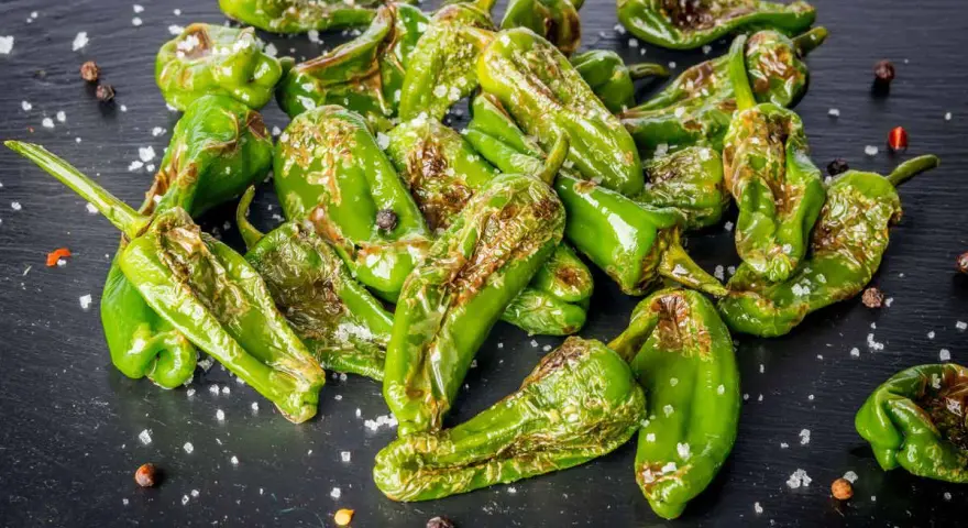 Friggitelli verdi, cotti in friggitrice ad aria, cosparsi di sale grosso e pepe nero su una superficie scura.