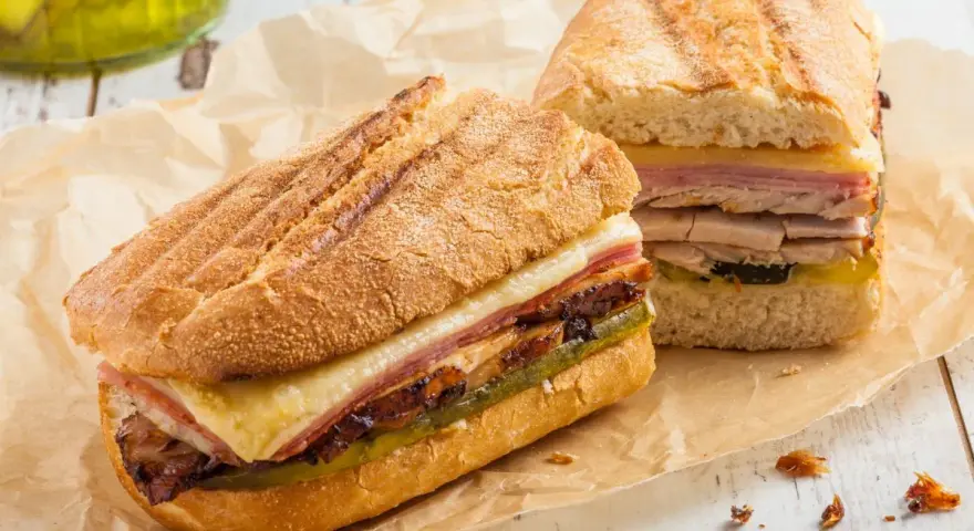 Dos sándwiches cubanos a la parrilla con capas de carne, queso derretido y pepinillos.