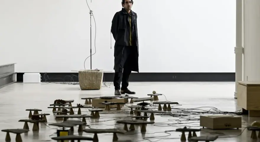 Tarek Atoui, artiste, se tient au milieu d'une installation sonore avec de nombreuses petites structures en pierre et en bois reliées par des câbles.