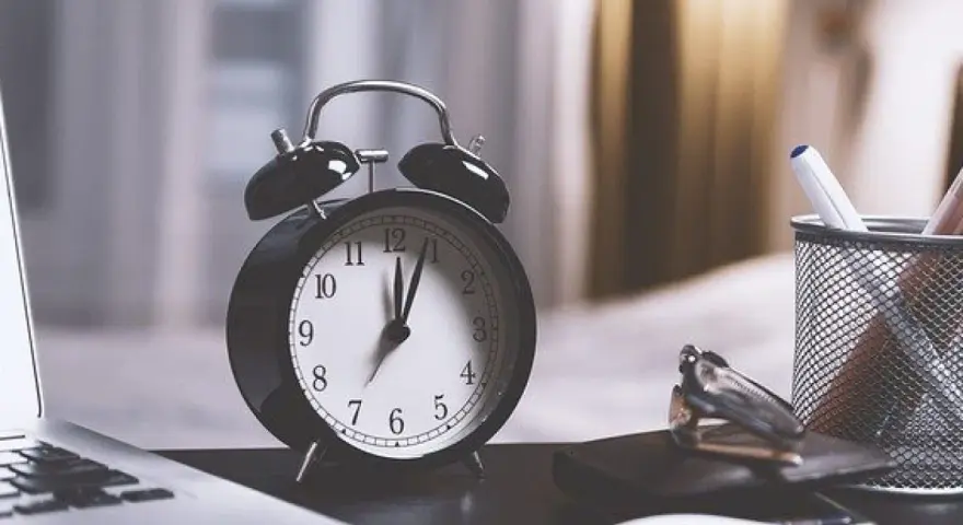 Budzik na biurku obok laptopa i notesu. Zastanawiasz się, po jakim czasie chwilówki oddają sprawę do sądu? Czas ucieka.