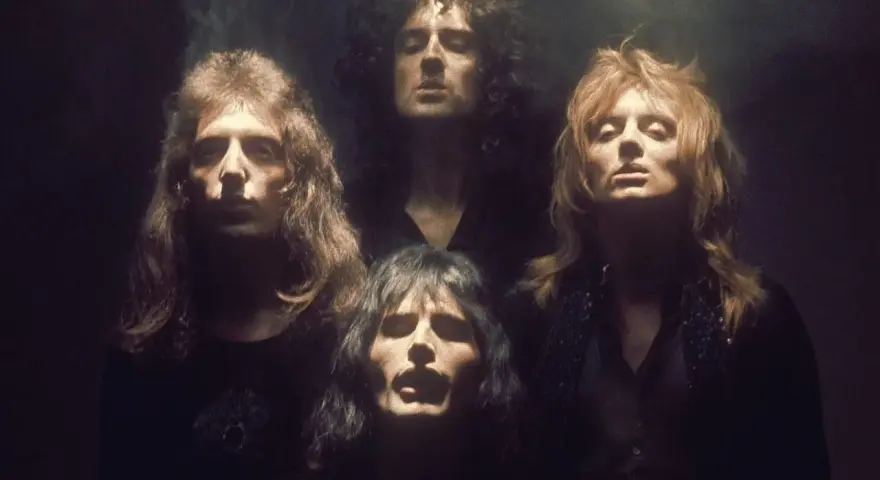 Czterech członków zespołu Queen w mrocznym klimacie, jakby przygotowujących się do wykonania "Bohemian Rhapsody". Ich spojrzenia sugerują głęboką interpretację.