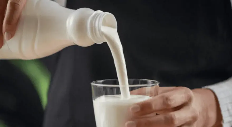 Kefir, naturalny probiotyk, pomaga zwalczać grzybicę jamy ustnej. Biały napój leje się z butelki do szklanki.