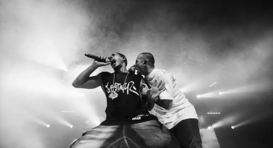 Deux rappeurs en pleine performance, l'un tenant un micro, l'autre le soutenant. Une scène intense qui illustre la puissance du hip hop en France.