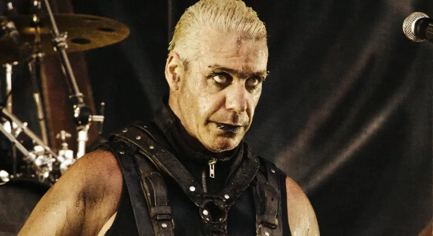 Till Lindemann młody, w skórzanym gorsecie, z mokrymi włosami i intensywnym spojrzeniem, gotowy do występu na scenie.