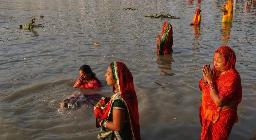 Mujeres rezan en el río Ganges, con vestimentas coloridas y el agua hasta la cintura.