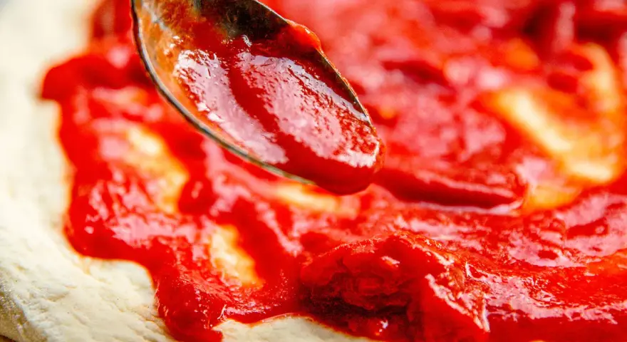 Eine Löffelspitze verteilt die original italienische pizzasauce auf einem Pizzateig.