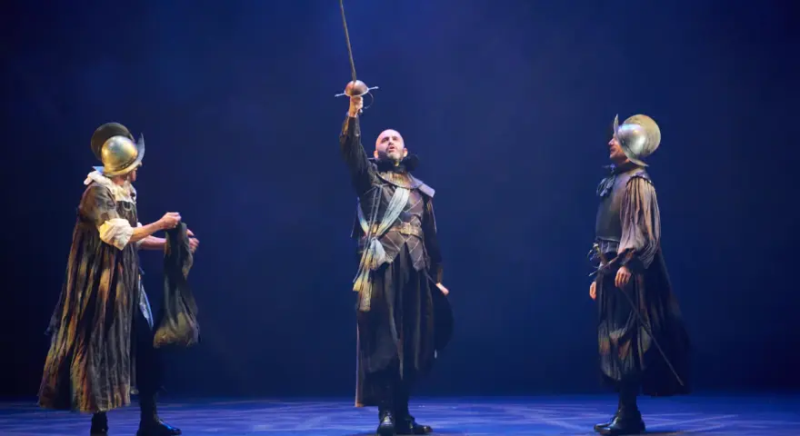 Tres hombres con armadura y espadas en un escenario. El del centro levanta su espada. Escena de "El alcalde de Zalamea".