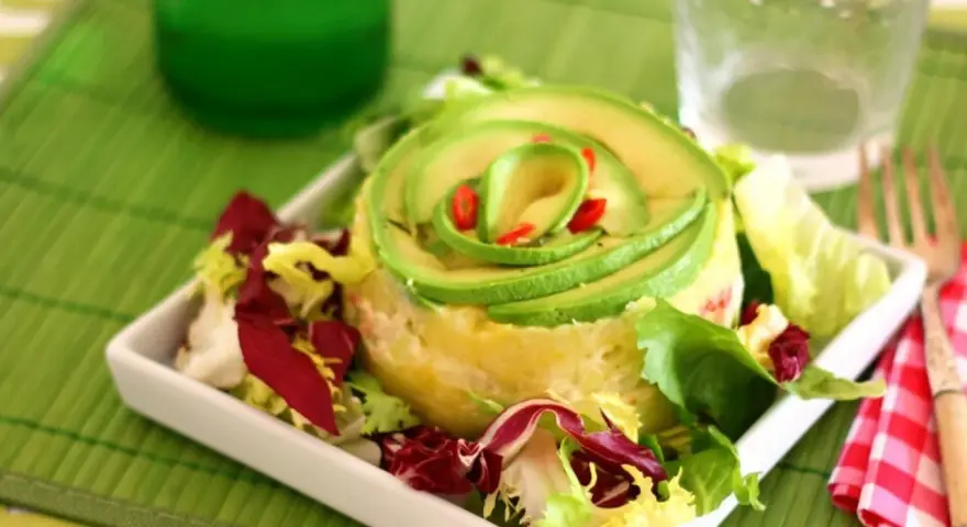 Causa limeña con aguacate en espiral y ensalada fresca, servida en plato blanco.