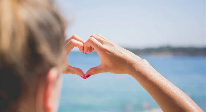 Message après premier rendez-vous avec un homme : un cœur formé par des mains mouillées sur fond de mer bleue.