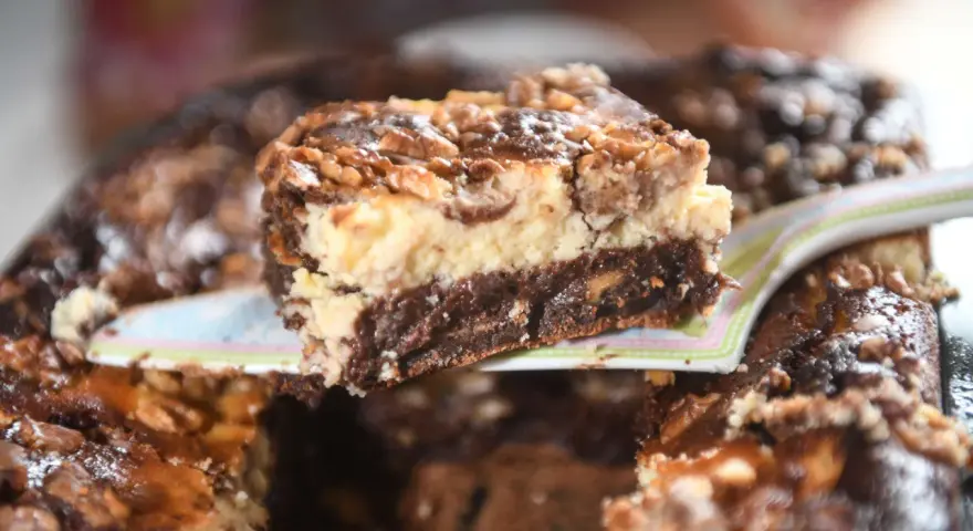 Ein Stück saftiger "friss dich dumm kuchen vom blech" mit Schichten aus Schokolade, Käsekuchen und Nüssen wird serviert.