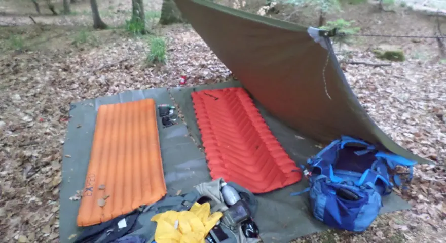 Zwei Isomatten, ein Tarp und Rucksäcke liegen bereit, um unter freiem Himmel zu schlafen.