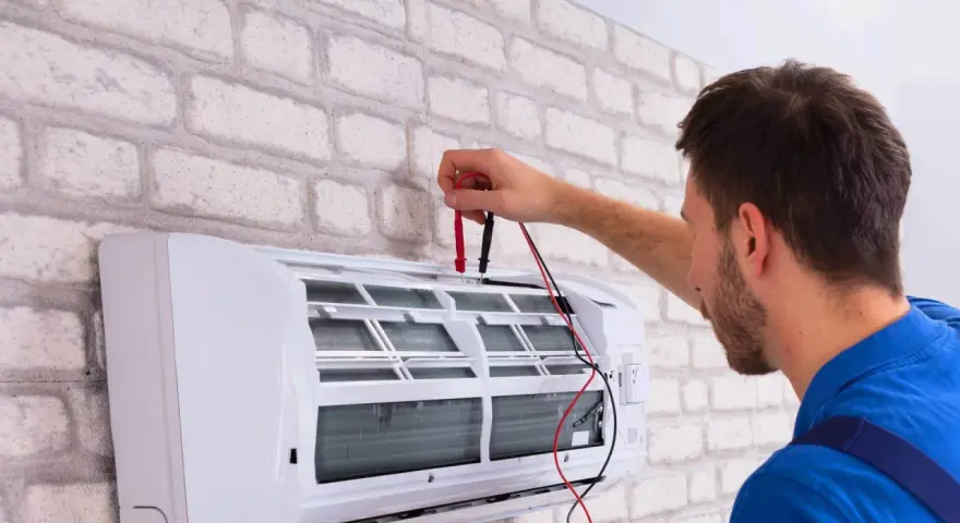 Sprawdź, jaka jest odgrzybianie klimatyzacji cena. Technik z miernikiem przy białej klimatyzacji.
