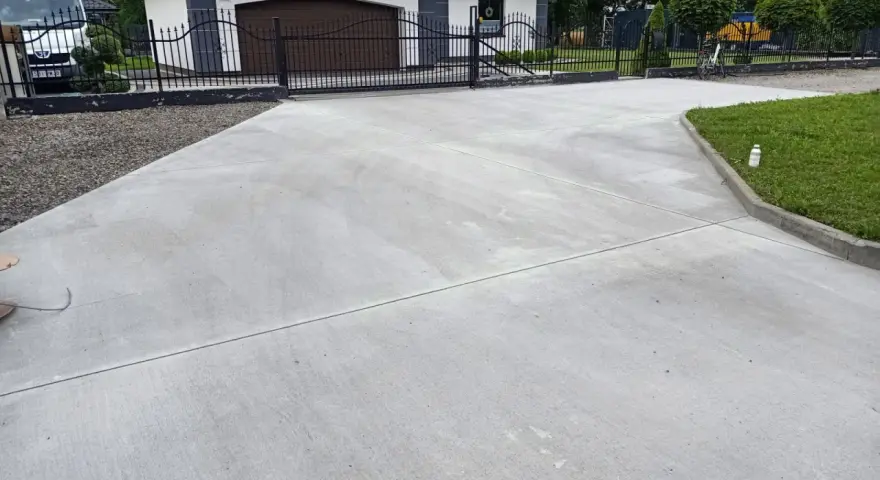 Nowy podjazd z betonu przed domem z garażem i bramą.