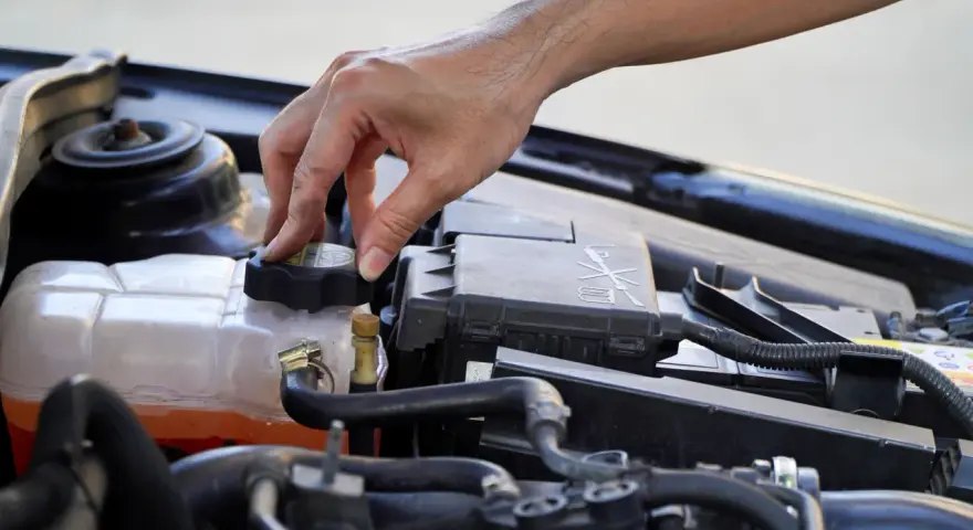 A hand twists the cap on a car's coolant reservoir, a step in learning how to dispose of antifreeze safely.