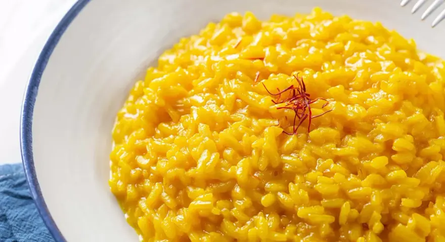 Un cremoso risotto alla milanese, giallo intenso grazie allo zafferano, guarnito con fili rossi.
