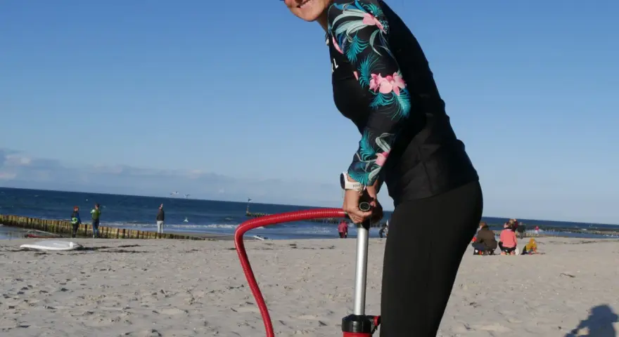 Frau pumpt SUP auf. Am Strand bereitet sie sich auf Wassersport vor.