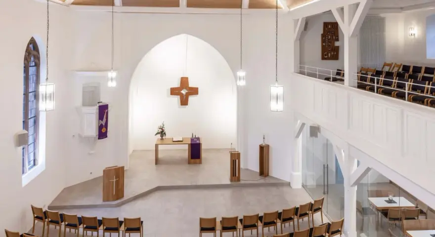 Moderner Aufbau evangelische Kirche mit Holzkreuz, Altar, Kanzel und vielen Sitzplätzen.