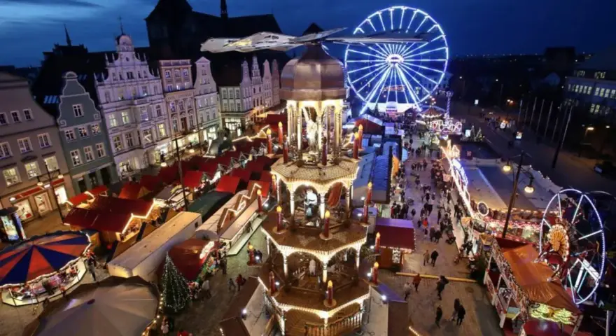 Ein beleuchteter Weihnachtsmarkt Mecklenburgische Seenplatte mit Riesenrad, Pyramide und Buden.