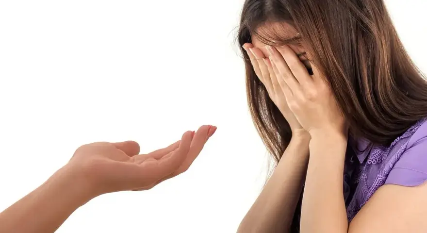 Kobieta płacze, zakrywając twarz dłońmi. Wyciągnięta dłoń oferuje wsparcie, symbolizując trudny moment, jak przyznać się do kłamstwa.