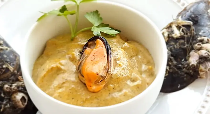 Paté de mejillones cremoso en cuenco blanco, decorado con perejil y mejillones enteros al lado.