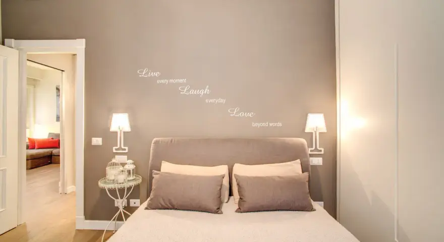 Camere da letto belle con citazione "Live, Laugh, Love" sulla parete. Letto accogliente con cuscini e lampade moderne.