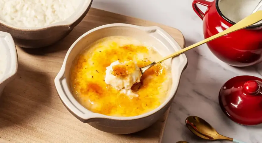 Delicioso arroz con leche asturiano con una capa crujiente de caramelo. Una cuchara dorada levanta una porción cremosa.