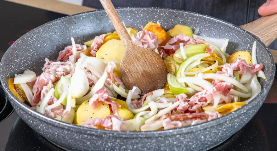 Zutaten für einen herzhaften Hamburger Pannfisch werden in einer Pfanne vermischt: Kartoffeln, Speck und Zwiebeln.