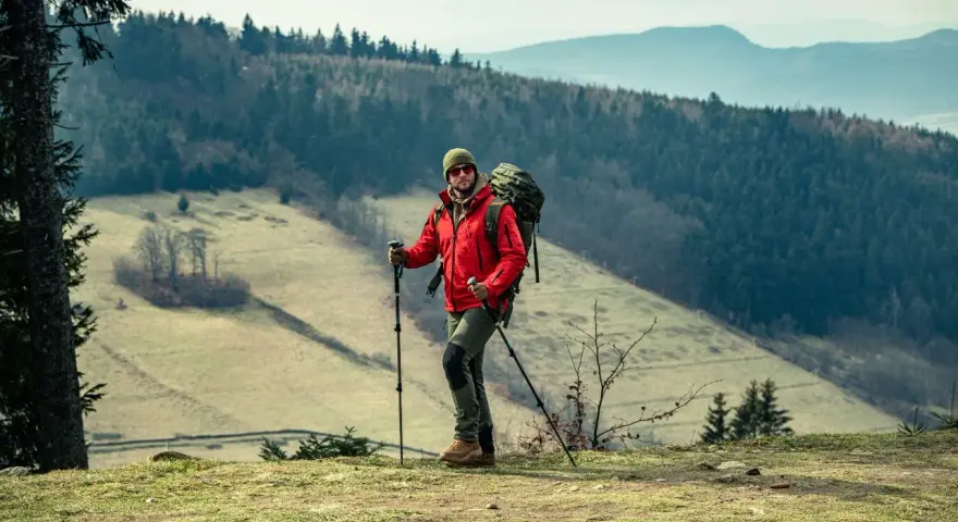 Mężczyzna w czerwonej kurtce i z plecakiem, gotowy do nordic walking. Jak zacząć? Wskazówki dla początkujących.