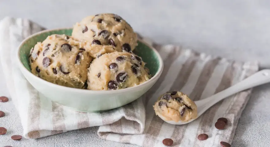 Schüssel mit köstlichem Cookie-Teig ohne Ei und Schokostückchen, bereit für den Ofen. Ein Löffel voll Teig liegt daneben.