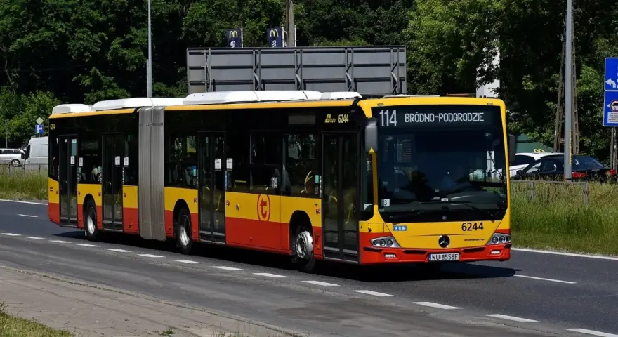 Autobus 114 jedzie ulicą w słoneczny dzień.