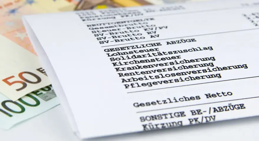 Nahaufnahme einer Entgeltabrechnung mit Euro-Scheinen. Die Abrechnung zeigt Brutto- und Nettobeträge sowie gesetzliche Abzüge wie Lohnsteuer und Versicherungen.